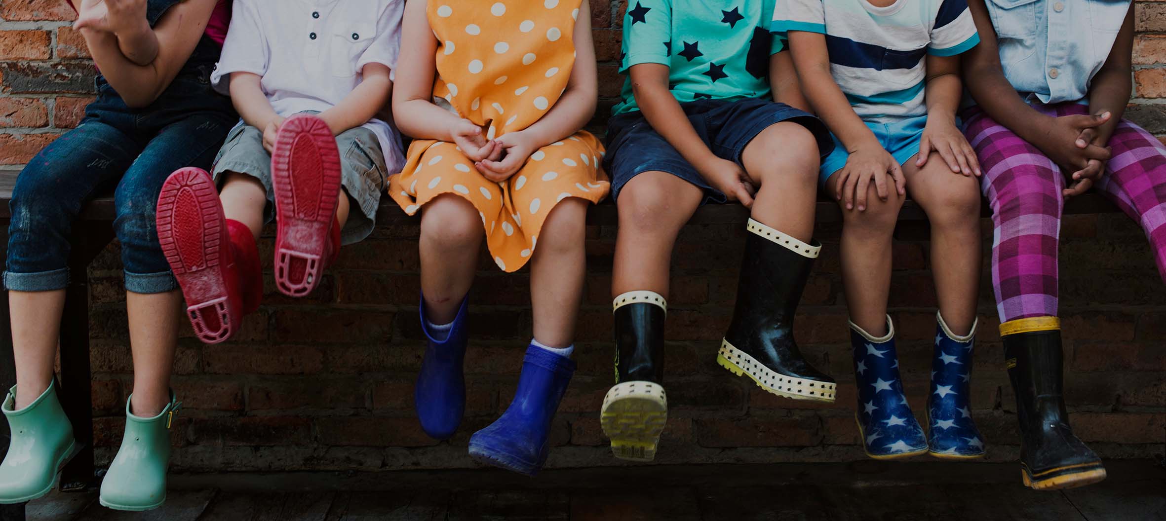 Vista parcial de piernas de niños sentados con botas de agua de diferentes colores y estampados