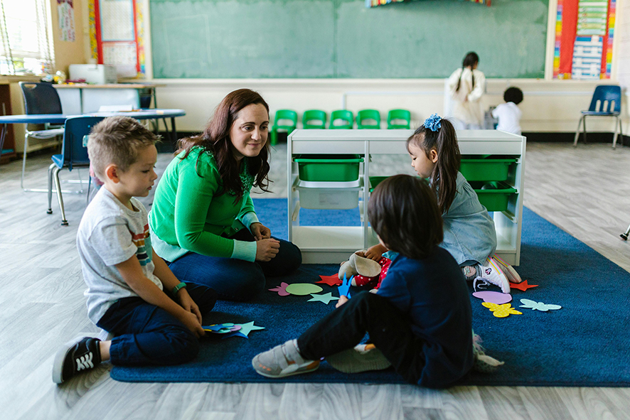 Imagen de una docente sentada en el suelo con tres alumnos realizando una actividad