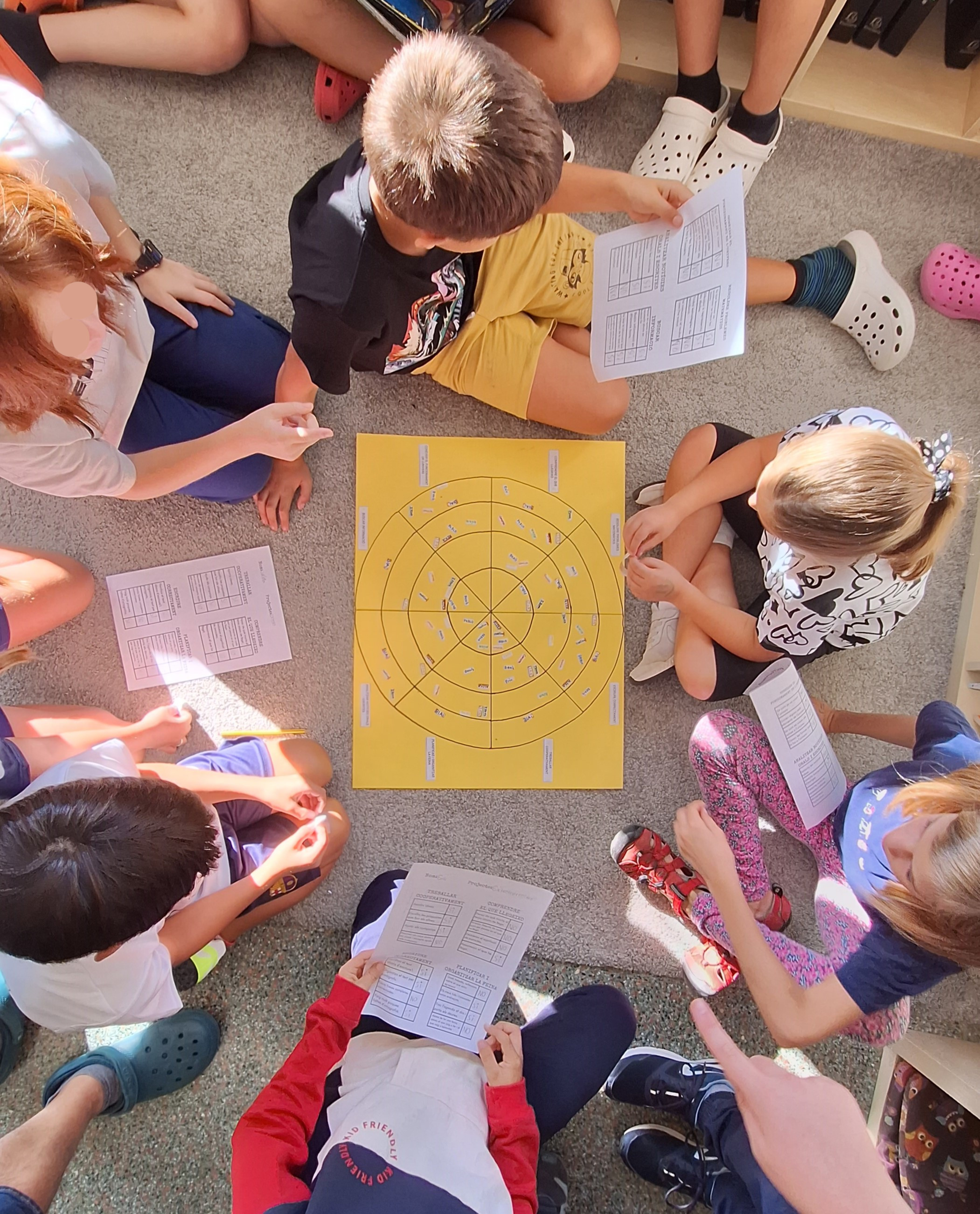 Un grup d'alumnes mirant les activitats a realitzar, asseguts en el pati de l'escola