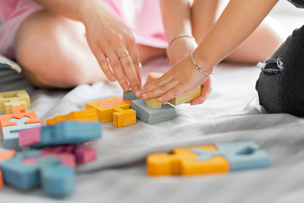 Manos de niños trabajando con piezas de madera, acompanyados por una maestra