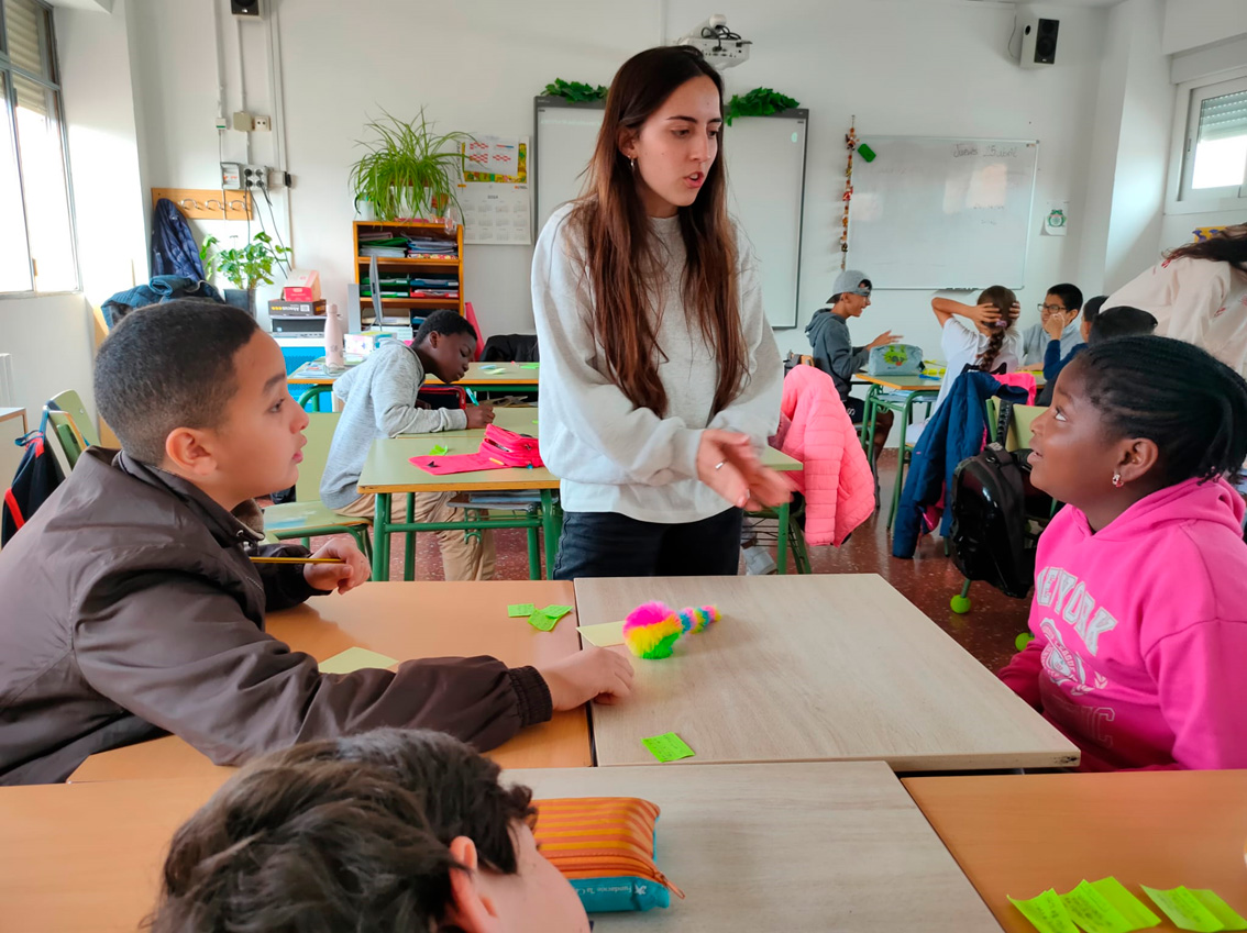 Imatge d'una classe de primària on la docent en pràctiques explica com fer l'activitat a uns alumnes