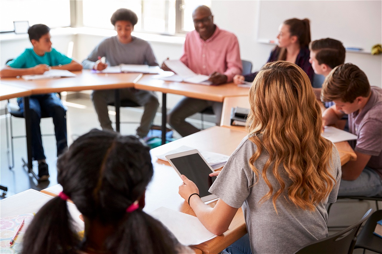 Alumnos y docente sentados en una mesa redonda, interactuando